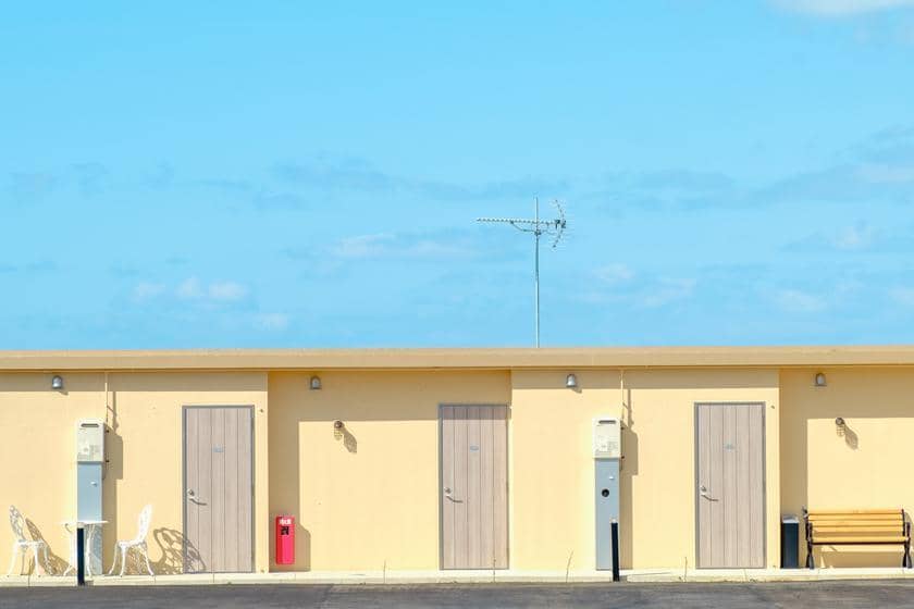 建物の外観が明るい空を背景に描かれており、複数の扉が整列している