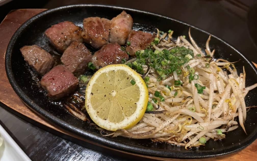 鉄板に乗せられたステーキともやし、輪切りのレモンが添えられている