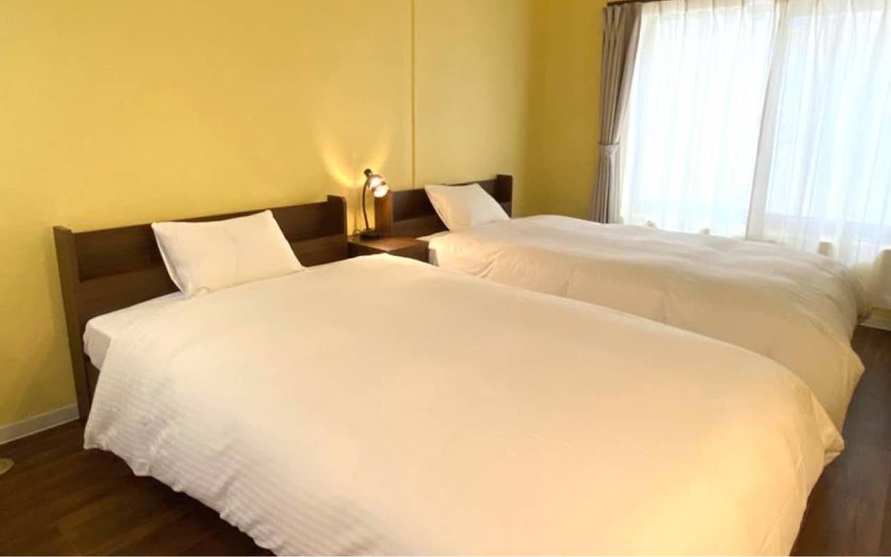 黄色い壁を背景に、2つのクイーンサイズベッドが並ぶ広々としたベッドルーム