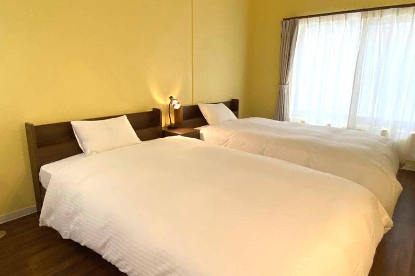 2つの木製フレーム付きベッドとテレビが設置された、ラベンダーカラーの壁の部屋