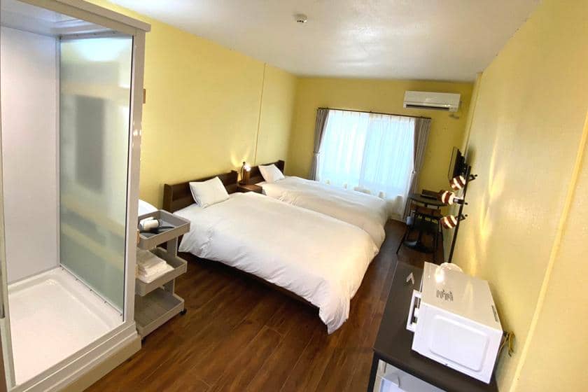 黄色の壁で彩られたツインベッドルーム。柔らかい白いカーテンから自然光が入り込む