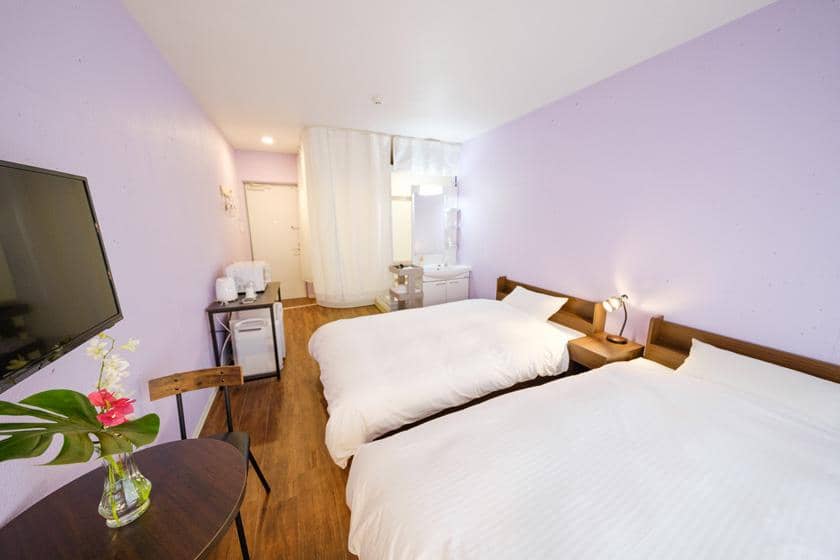 客室全体の様子。薄紫の壁と白いカーテン、洗面台が見える