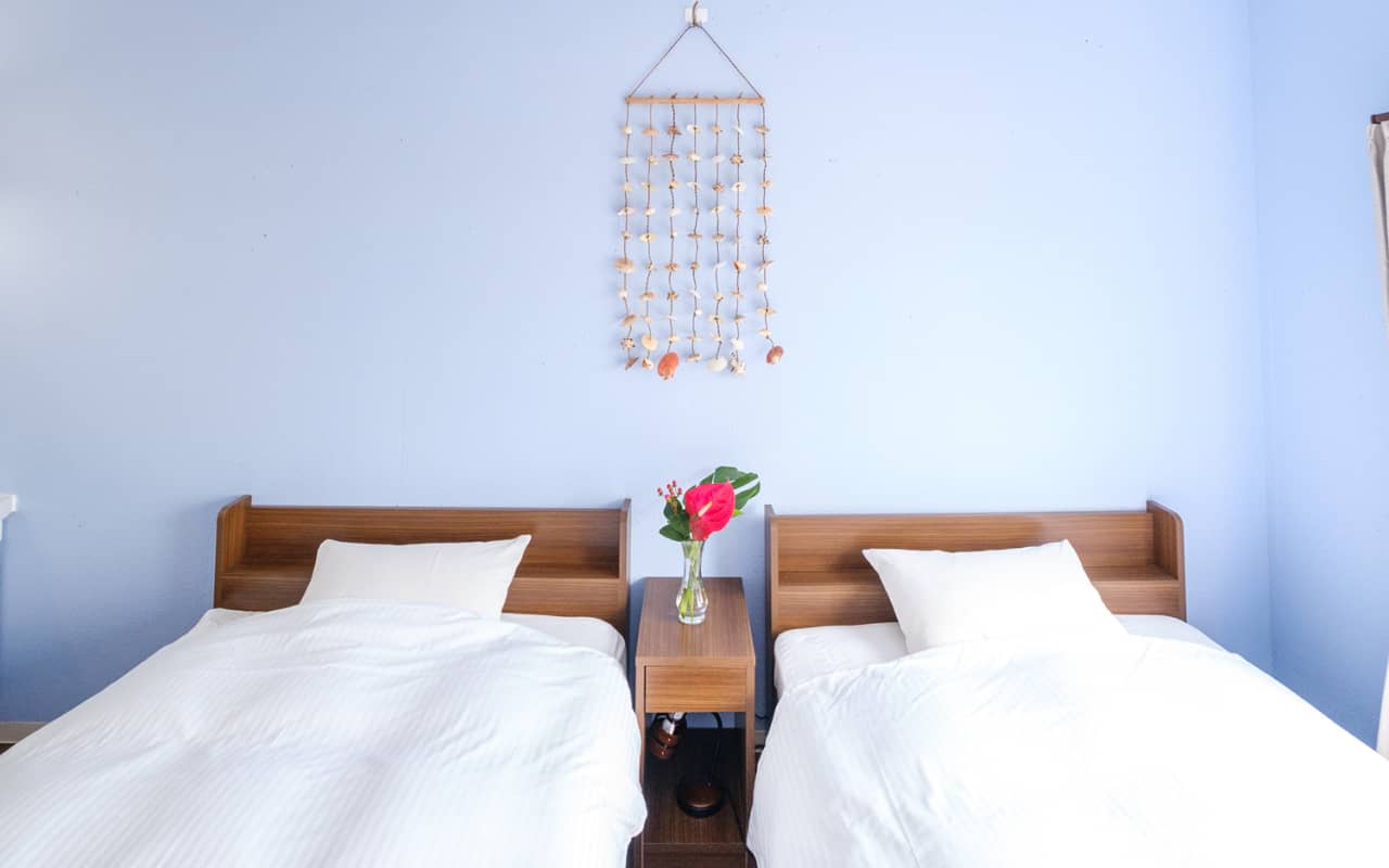 青い壁に面したツインベッドルーム、中央に花の飾られた小さなテーブルが置かれている