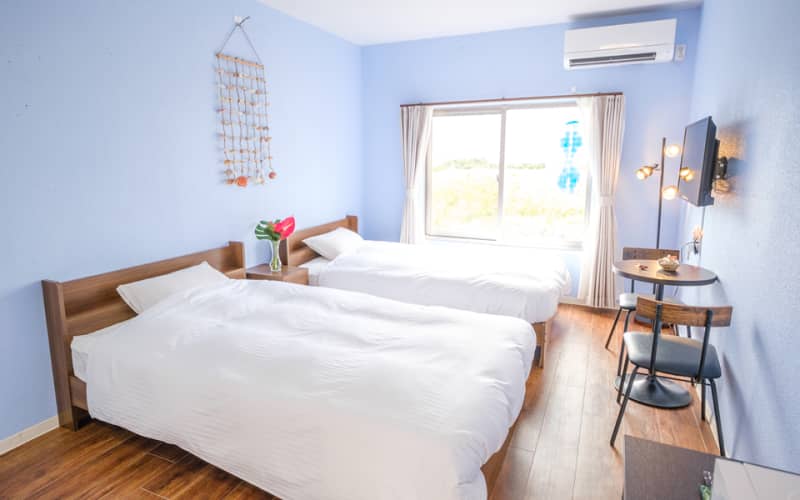 窓からの景色と青い壁が特徴的な明るいツインベッドルーム。モダンな照明と装飾がアクセント